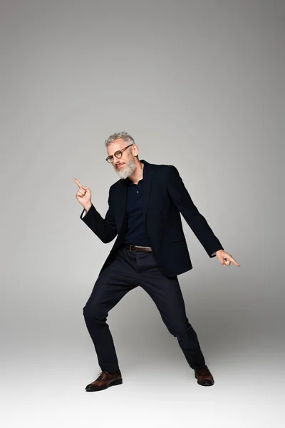 Pleine longueur de l'homme d'âge moyen en lunettes et costume dansant sur gris — Photo de stock