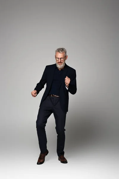 Longitud completa de hombre de mediana edad complacido en gafas y traje bailando en gris - foto de stock