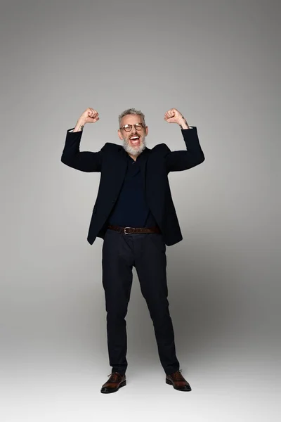 Pleine longueur de l'homme d'âge moyen excité dans des lunettes et costume se réjouissant sur le gris — Photo de stock