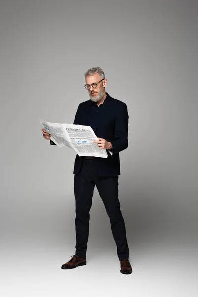 Comprimento total do homem de meia idade em óculos e terno lendo notícias econômicas em cinza — Fotografia de Stock