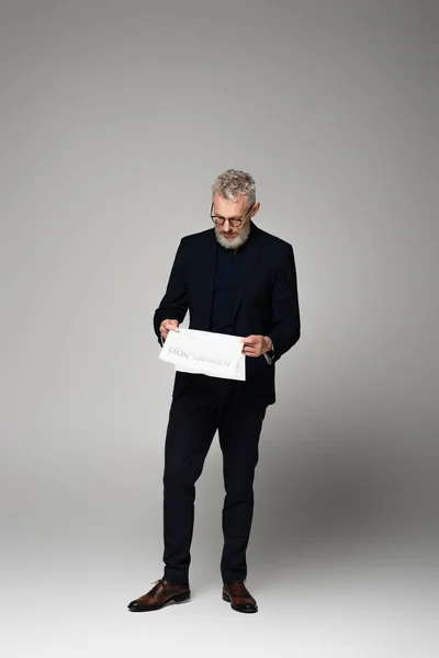 Pleine longueur d'homme d'affaires d'âge moyen dans des lunettes de lecture journal sur gris — Photo de stock