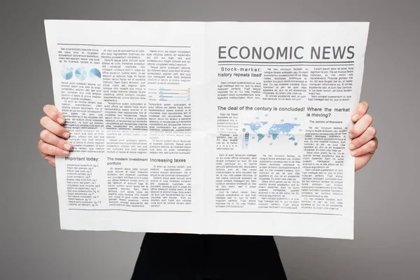 Hombre cubriendo la cara mientras lee noticias económicas aisladas en gris - foto de stock