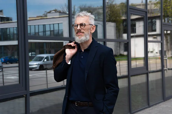 Mature man with grey hair holding leather bag while standing outside — Stock Photo