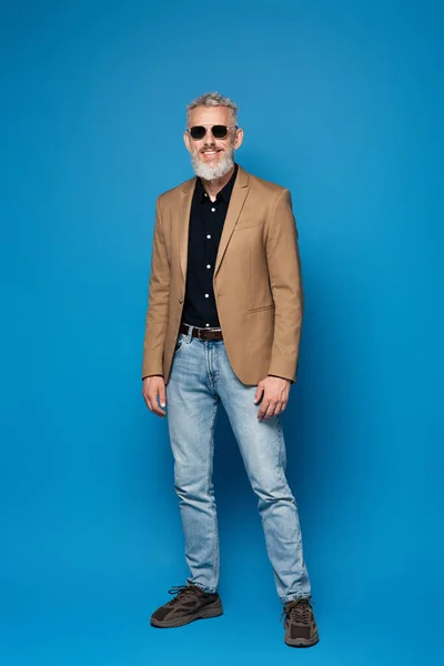 Volle Länge des glücklichen Mannes mittleren Alters in Sonnenbrille posiert auf blau — Stockfoto