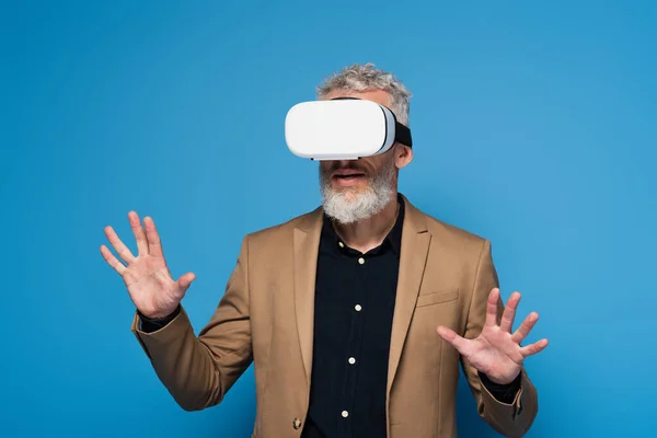 Middle aged man in vr headset gesturing isolated on blue — Stock Photo