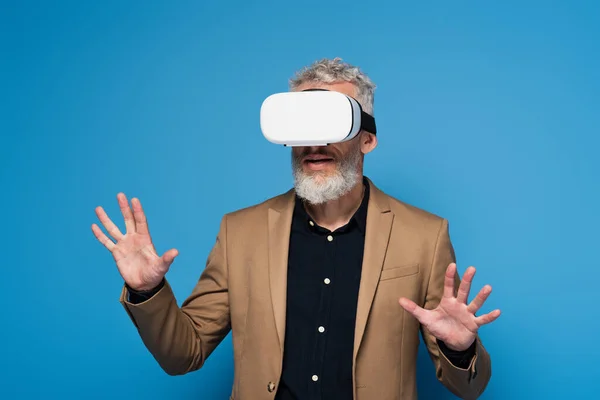 Hombre de mediana edad en auriculares vr gesto aislado en azul - foto de stock