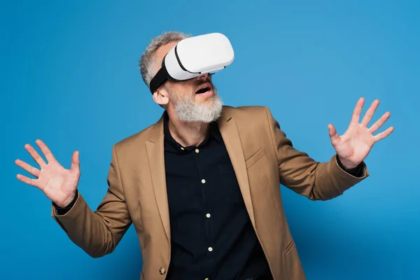 Surprised middle aged man in vr headset gesturing on blue — Stock Photo