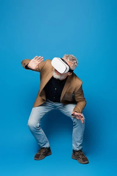 Pleine longueur de l'homme d'âge moyen en vr casque accroupi sur bleu — Photo de stock