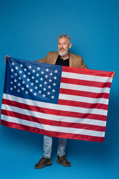 Toute la longueur de barbu homme d'âge moyen debout avec drapeau de l'Amérique sur le bleu — Photo de stock