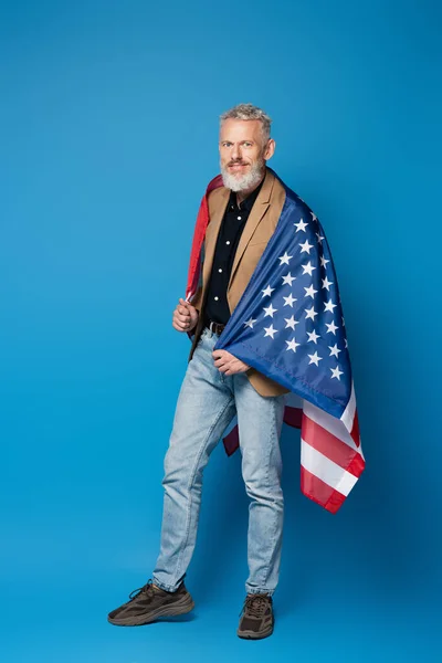 Comprimento total do homem positivo de meia-idade de pé com bandeira americana em azul — Fotografia de Stock