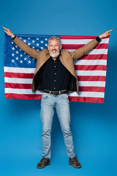 Pleine longueur de heureux homme d'âge moyen debout avec drapeau américain sur bleu — Photo de stock