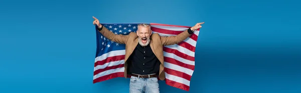 Hombre de mediana edad emocionado de pie con bandera americana en azul, bandera - foto de stock