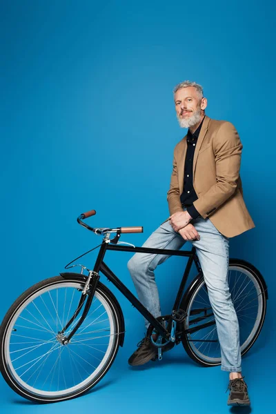 Full length of pleased middle aged man sitting on bicycle on blue — Stock Photo