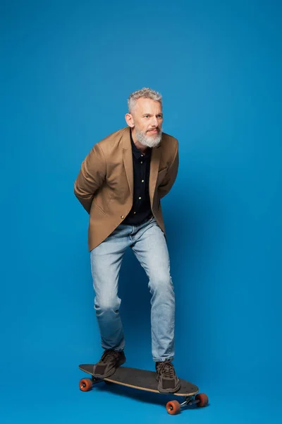 Full length of middle aged man riding on longboard on blue — Stock Photo