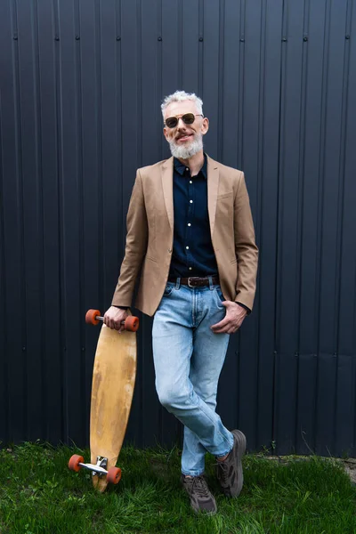 Voller Länge fröhlicher Mann mittleren Alters mit Sonnenbrille und Longboard draußen — Stockfoto