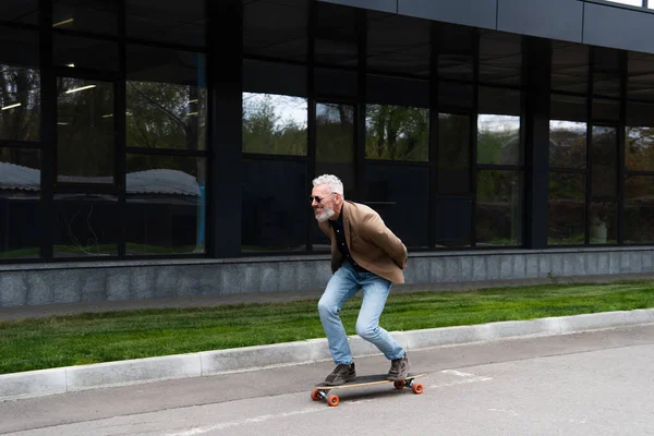 Full length of happy middle aged man in sunglasses riding longboard outside — Stock Photo