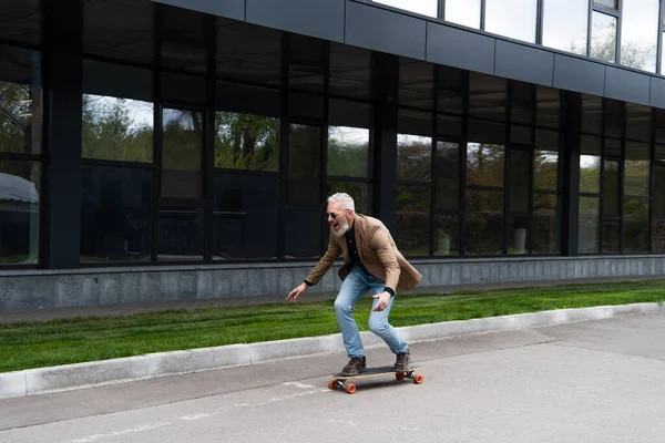 Pleine longueur de l'homme d'âge moyen positif dans les lunettes de soleil équitation longboard à l'extérieur — Photo de stock