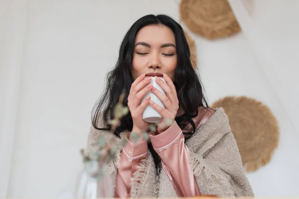 Giovane donna asiatica che tiene in mano una tazza di caffè e gode dell'aroma in camera da letto — Foto stock