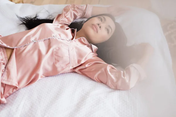 High angle view of young asian woman lying outside curtain on white linen with outstretched hands in bedroom — Stock Photo