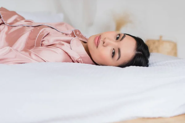Giovane donna asiatica sdraiata sul letto e guardando la fotocamera in camera da letto — Foto stock