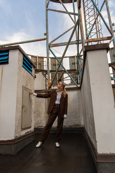 Full length of trendy model in sunglasses and brown suit posing on rooftop — Stock Photo