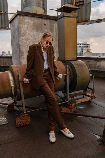 Blondes Model in Sonnenbrille und trendigem braunem Anzug posiert auf dem Dach — Stockfoto