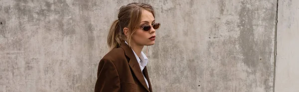 Verträumtes junges Model in stylischer Sonnenbrille und trendigem Anzug posiert auf Dach, Banner — Stockfoto