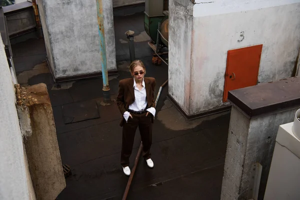 High angle view of stylish blonde model posing with hands in pockets on rooftop — Stock Photo