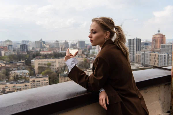 Jeune femme tenant un verre de vin blanc et posant avec paysage urbain sur fond flou — Photo de stock