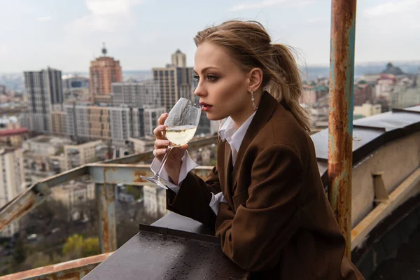 Young woman drinking wine on rooftop with cityscape on blurred background — Stock Photo