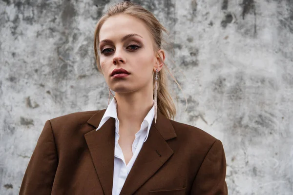 Giovane modella in blazer marrone alla moda in posa vicino al muro di cemento — Foto stock