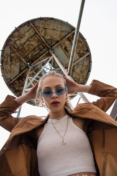 Low angle view of trendy model in blue sunglasses looking at camera near construction on rooftop — Stock Photo