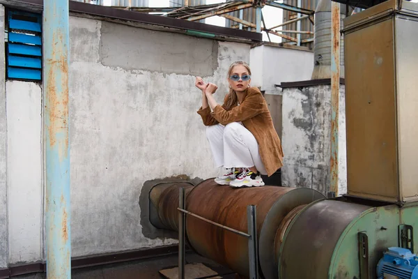 Full length of young stylish woman in trendy outfit and blue sunglasses posing on rusty construction — Stock Photo