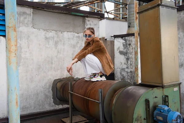 Full length of young model in stylish outfit posing on rusty construction — Stock Photo