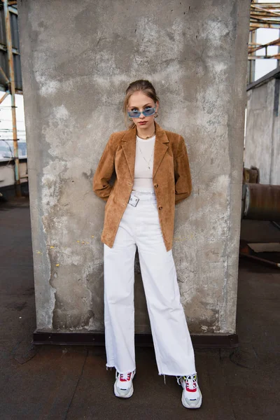 Full length of young model in blue sunglasses and stylish outfit posing near concrete wall — Stock Photo