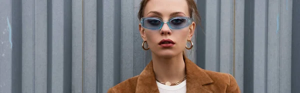 Mujer bonita en gafas de sol azules y pendientes posando fuera, pancarta - foto de stock