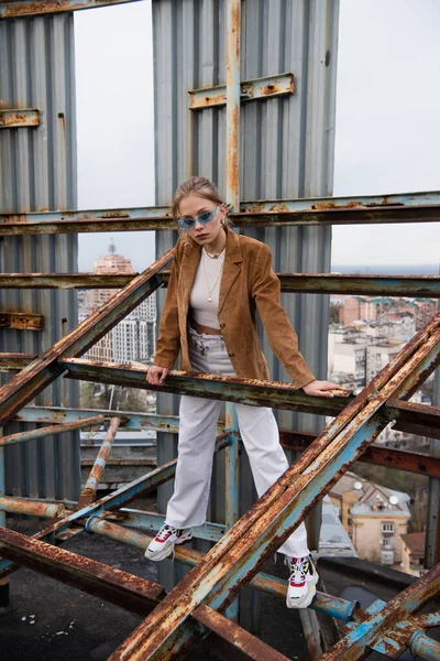 Full length of young and pretty woman in stylish outfit and sunglasses standing on weathered construction of rooftop — Stock Photo