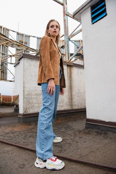 Comprimento total de jovem mulher em roupa elegante com jeans e tênis na moda em pé no telhado — Fotografia de Stock