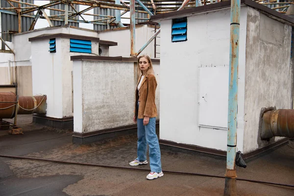 Full length of young model in stylish outfit with jeans and trendy sneakers standing on rooftop — Stock Photo