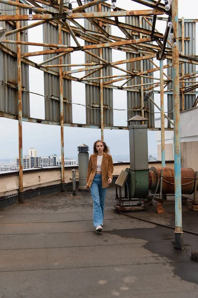 Pleine longueur de femme blonde en jeans denim et baskets élégantes marchant sur le toit — Photo de stock