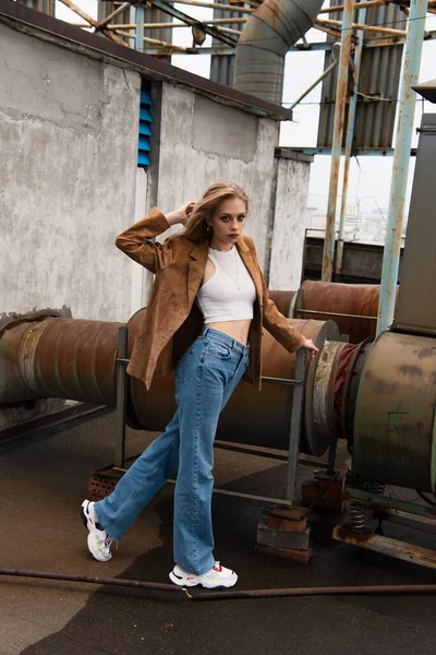 Longueur totale de jeune modèle en jeans denim et baskets posant sur le toit — Photo de stock