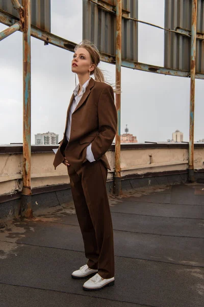 Full length of dreamy model in white shirt and brown suit standing with hands in pockets on rooftop — Stock Photo