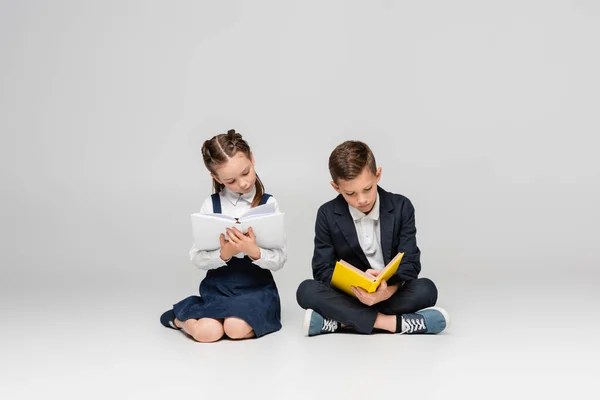 Alunos sentados e lendo livros sobre cinza — Fotografia de Stock