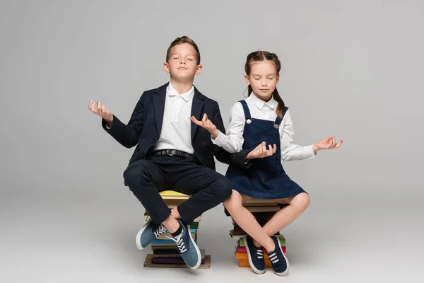 Schulkinder meditieren, während sie auf einem Stapel Bücher auf grau sitzen — Stockfoto