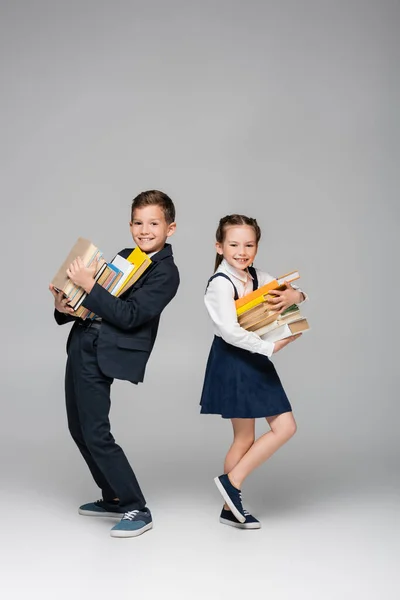 Glückliche Schulkinder mit einem Stapel Bücher auf grau — Stockfoto
