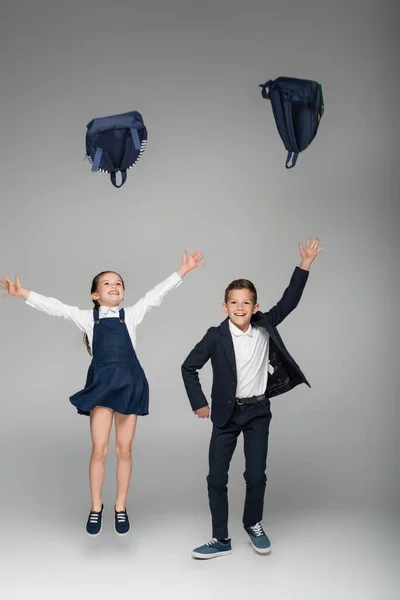 Meninos felizes jogando mochilas no ar em cinza — Fotografia de Stock