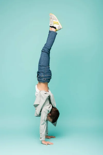 Garçon en jeans denim faisant handstand sur bleu — Photo de stock