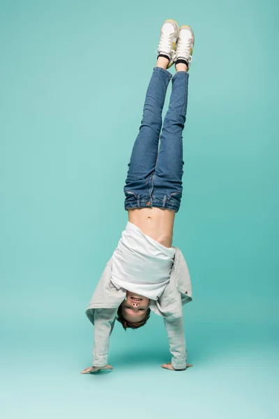 Happy boy in denim jeans doing handstand on blue — Stock Photo