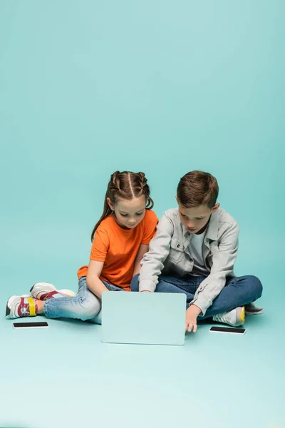 Kids using laptop near smartphones with blank screen on blue — Stock Photo