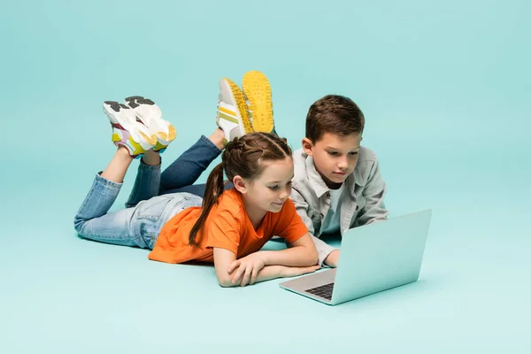 Kinder sehen sich Film auf Laptop an, während sie auf blauem Grund liegen — Stockfoto